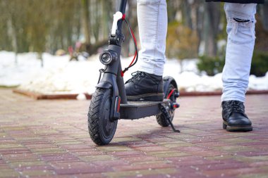 Elektrikli scooter yakın plan. Adam parkta elektrikli scooter 'ın yanında duruyor. İlkbahar parkında güzel bir scooter fotoğrafı.