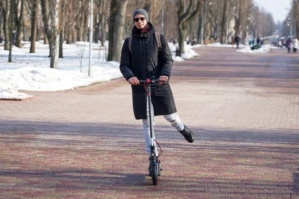 Guy Rides Electric Scooter Spring Park Wearing Warm Jacket Hat — Foto Stock