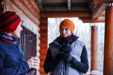 İki adam kayaktan sonra sohbet eder. Kışlık giysilerle ahşap bir evin balkonunda durup çay içip rahatlıyorlar. Alplerdeki bir kayak merkezinde iki adam.