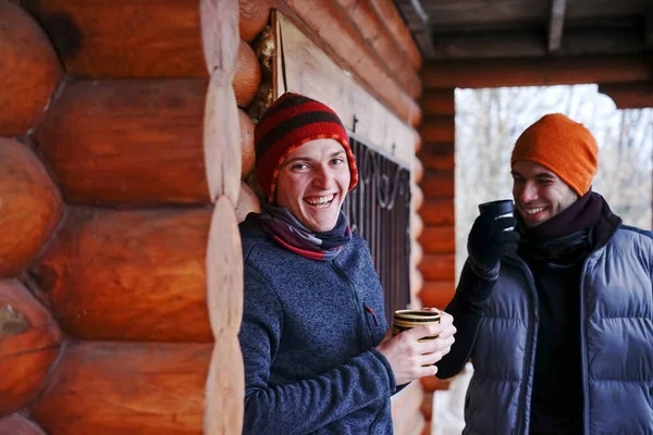 Two guys chat after skiing. They stand on the balcony of a wooden house in winter clothes, drink tea and relax. Porter of two guys in a ski resort in the alps