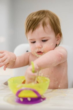 Komik küçük kız kaşık kullanmayı öğreniyor, elleriyle yemek yiyor.