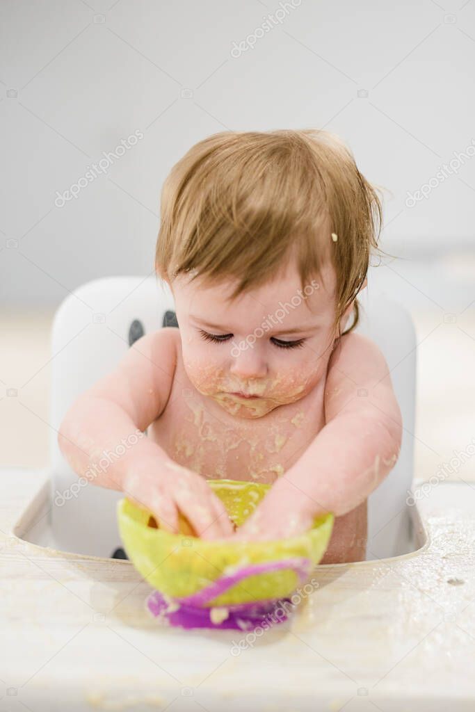 Smeary funny baby girl eating food with hands