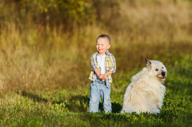 Mutlu gülümseyen sarışın çocuk çiftlikte köpek arkadaşıyla yürüyor.
