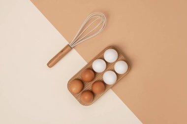 Tahta yumurta kutusunda yumurtalar ve bej kahverengi arka planda çırpma. Düz konum Üst Görünüm Kopyalama alanı.