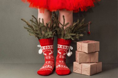 Süslü kırmızı yün çoraplı kadın bacakları, köknar dalları ve yeşil arka planda xmas hediyeleri. Mutlu Noeller ya da yeni yıl tatili, yaratıcı konsept.
