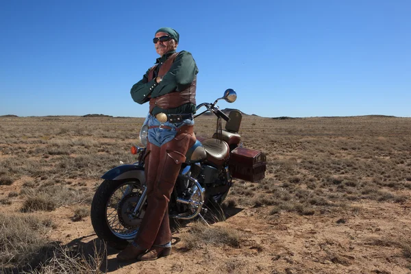 Bello pensionato nel deserto appoggiato alla moto Foto Stock Royalty Free