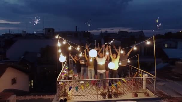 Фейерверки во время полуночной вечеринки многонациональной группы молодых людей, празднующих на крыше машут на дроне холдинг искрящийся огонь праздничное время счастливое событие красивые огни Городская ночь Новый год — стоковое видео