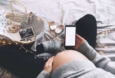 Boş beyaz bir ekranla el ele tutuşan hamile bir kadın. Müstakbel annenin karnına ultrason fotoğrafları ve tıbbi test raporlarıyla yakın çekim. Hamilelik kavramı, jinekoloji.