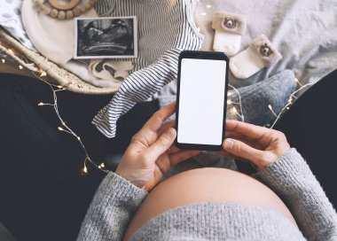 Boş beyaz bir ekranla el ele tutuşan hamile bir kadın. Müstakbel annenin karnına ultrason fotoğrafları ve tıbbi test raporlarıyla yakın çekim. Hamilelik kavramı, jinekoloji.