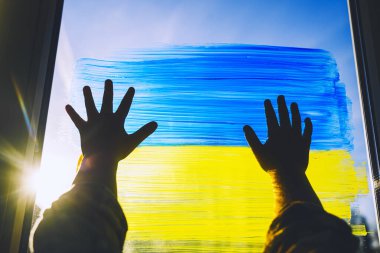 Çocuğun elleri pencereye Ukrayna 'nın sarı-mavi bayrağını çiziyor. Camda Ukrayna bayrağı olan küçük bir çocuğun elleri. Ukraynalıları ve çocukları destekleyin. Kavram simgesi, arkaplan.