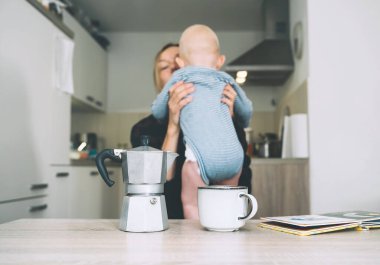 Uykusuz bir geceden sonra modern, yorgun bir anne ve küçük bir çocuk. Bebekli bitkin bir kadın mutfakta kahveyle oturuyor. Bebekle çalışan anne hayatı. Doğum sonrası depresyonu doğum izninde.