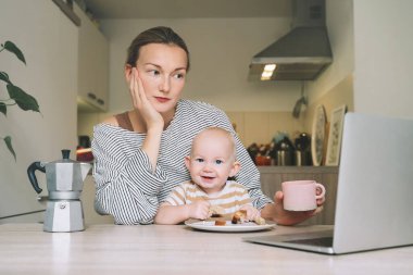 Mutfakta bebekle kahvaltı ederken kahve içmekten yorgun düşmüş genç bir anne. Uykusuz bir geceden sonra serbest çalışan anne ve çocuk. Doğum izninde evde çalışan ya da okuyan bir kadın