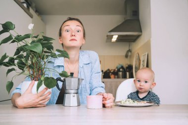 Çalışan bir anne ve küçük bir bebek. Kahveli ve bebekli genç bir kadın mutfakta kahvaltı yapıyor. Uykusuz bir geceden sonra modern serbest çalışan anne ve çocuğu. İş hayatı mı, iş aile dengesi mi?