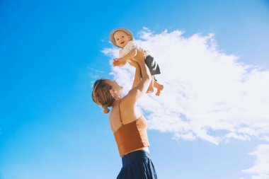 Anne bebeği mavi gökyüzüne fırlatıyor. Dışarıda mutlu bir aile. Anne ve bebek yazın doğada. Olumlu insani duygular ve duygular.