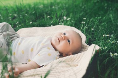 Yazın açık havada yeşil çimlerin üzerinde battaniyeye uzanmış sevimli mutlu bir bebek. 3 aylık çıplak ayaklı bir bebek doğada. Aile ve çocukluk eko sürdürülebilir yaşam tarzı kavramı.