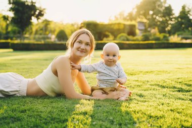 Genç anne ve bebek yazın parkta oynuyorlar. Güzel anne ve çocuk dışarıda. Çocuklu ebeveynler birlikte vakit geçirir. Güneş ışığında mutlu ve sağlıklı bir aile. Çevresel sürdürülebilir yaşam tarzı. Pozitif duygular.