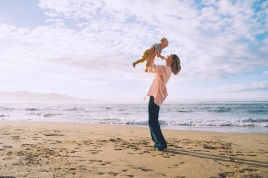 Anne ve küçük çocuğu kumsalda oynuyorlar ve birlikte eğleniyorlar. Dışarıda mutlu bir aile. Anne ve bebek yazın doğada. Olumlu insani duygular ve duygular. Deniz kıyısında aile tatili.