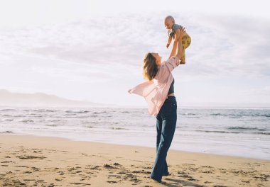 Anne ve küçük çocuğu kumsalda oynuyorlar ve birlikte eğleniyorlar. Dışarıda mutlu bir aile. Anne ve bebek yazın doğada. Olumlu insani duygular ve duygular. Deniz kıyısında aile tatili.