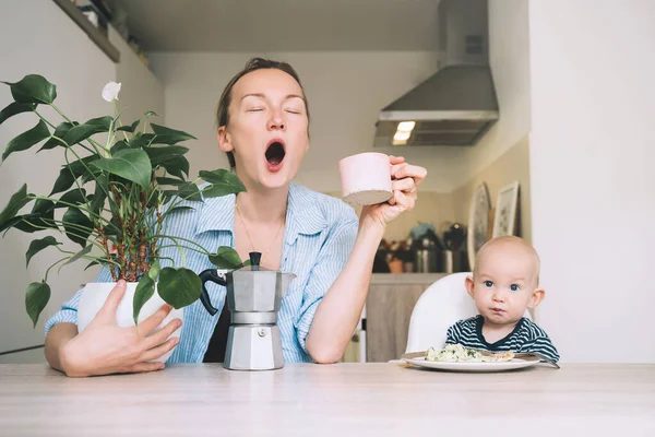 Çalışan bir anne ve küçük bir bebek. Kahveli ve bebekli genç bir kadın mutfakta kahvaltı yapıyor. Uykusuz bir geceden sonra modern serbest çalışan anne ve çocuğu. İş hayatı mı, iş aile dengesi mi?
