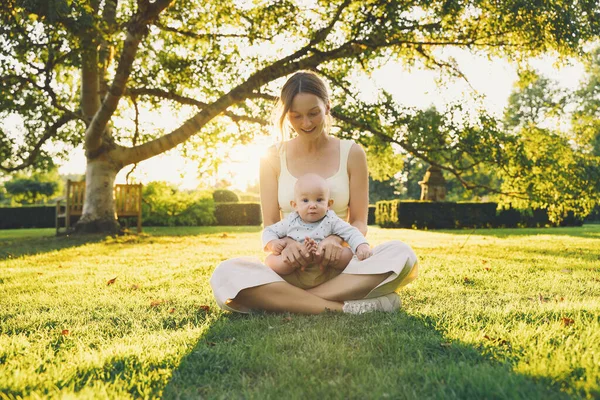 Genç anne ve bebek yazın parkta oynuyorlar. Güzel anne ve çocuk dışarıda. Çocuklu ebeveynler birlikte vakit geçirir. Güneş ışığında mutlu ve sağlıklı bir aile. Çevresel sürdürülebilir yaşam tarzı. Pozitif duygular.