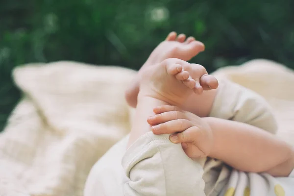 Baby tiny cute feet in green grass outdoors. Baby lying on blanket at summer on nature.