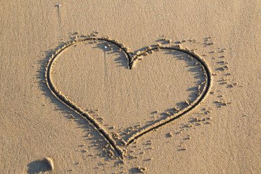 Kalp arka planda bir kumsalın kumunu çiziyor. Romantik alan.
