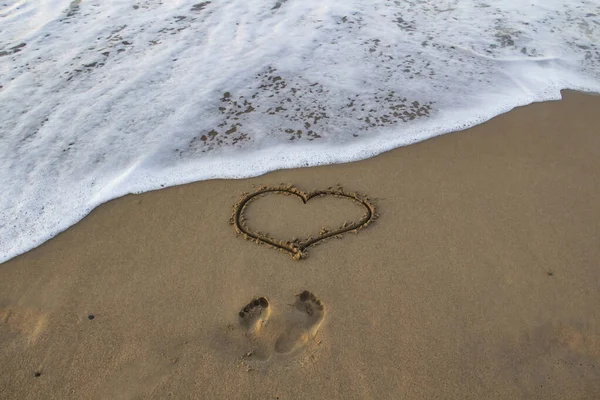 Kalp kumda çizilmiş, sahilde ayak izleri ve önünde deniz köpüğü var..