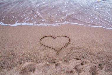 Kumsalda kumların üzerinde dalgalar ve kumların üzerinde bir kalp var. Dalgaların güzel manzarası