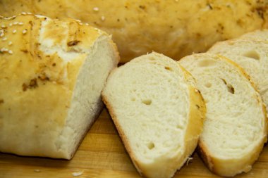 Evde un ile pişirilmiş buğday ekmeği. Ahşap tahta üzerinde arka planda dilimlenmiş ekmek. GDO 'suz yemek. Baharatlı ev yapımı ekmek..