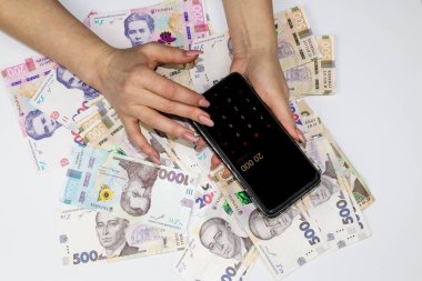 Cep telefonunda kadın eli hesap makinesinde 20.000 sayıyor. Arka planda 200, 500 ve 1000 'e kadar binlerce Hryvnia banknotu var. Ukrayna 'nın parası.