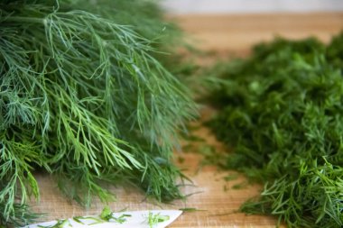 Tahtada doğranmış dereotu. Arka planda tahta bir bıçakla ev yapımı doğranmış dereotu hazırlamak. Tahtada yeşil baharatlı taze dereotu