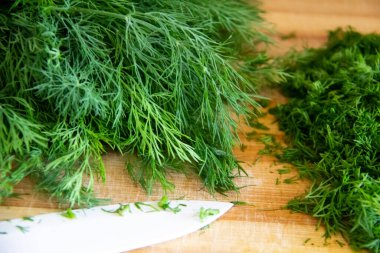 Tahtada doğranmış dereotu. Arka planda tahta bir bıçakla ev yapımı doğranmış dereotu hazırlamak. Tahtada yeşil baharatlı taze dereotu