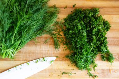 Tahtada doğranmış dereotu. Arka planda tahta bir bıçakla ev yapımı doğranmış dereotu hazırlamak. Tahtada yeşil baharatlı taze dereotu