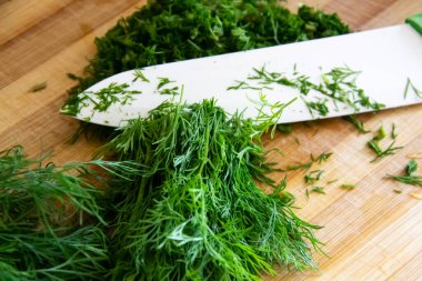 Tahtada doğranmış dereotu. Arka planda tahta bir bıçakla ev yapımı doğranmış dereotu hazırlamak. Tahtada yeşil baharatlı taze dereotu