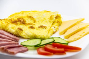 Lezzetli kahvaltı ya da omletli omlet sosis, domates, salatalık ve beyaz tabakta peynir parçaları..