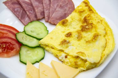 Lezzetli kahvaltı ya da omletli omlet sosis, domates, salatalık ve beyaz tabakta peynir parçaları..