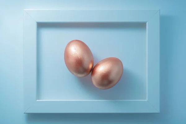 Par de ovos dourados emoldurados em fundo azul pastel. Composição contemporânea de páscoa de arte fina. Flat lay, vista superior, espaço de cópia. — Fotografia de Stock