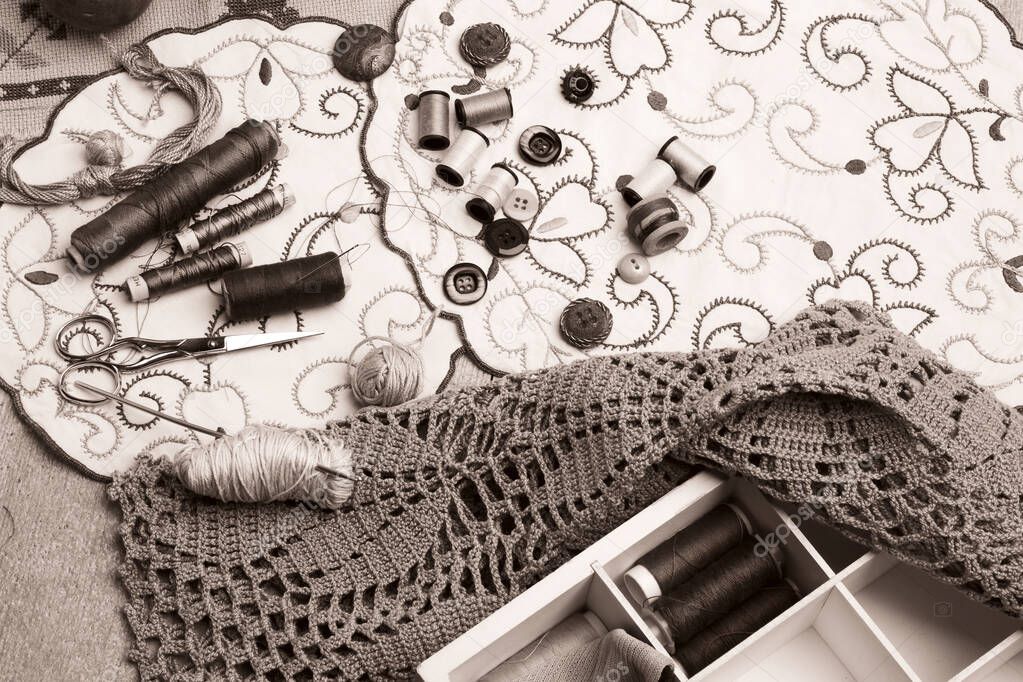 Set of sewing and embroidery supplies on a table: sewing thread, buttons, crochet, embroidered doiles, scissors. Retro effect , monochrome photography