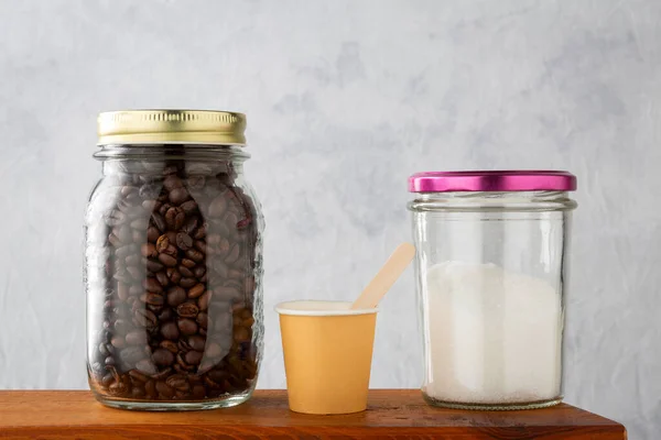 Coffe and sugar in glass jars, paper cup and wooden scoop. For a coffee break with ecological and recyclable materials.