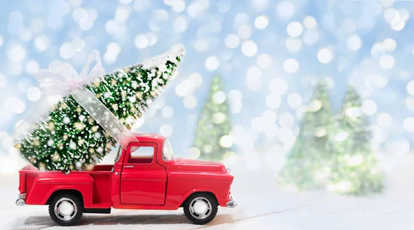 Piros autó szállító díszített karácsonyfa egy kék havas háttér. — Stock Fotó