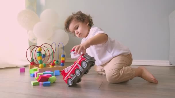 A kisfiú színes játékokkal játszik otthon a padlón. Aranyos gyermek játszik autós játék — Stock videók