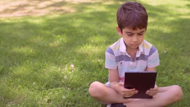 Garotinho Caucasiano Sentado Grama Verde Livre Usando Tablet Digital Close — Vídeo de Stock