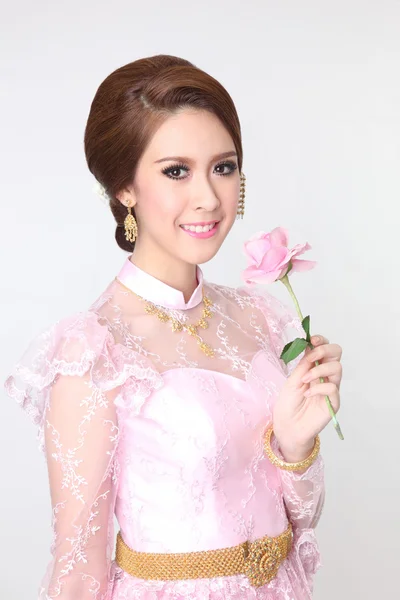 Elegante mode Aziatische vrouw poseren met creatieve chignon-kapsel en het dragen van roze Thaise jurk, houd roos — Stockfoto