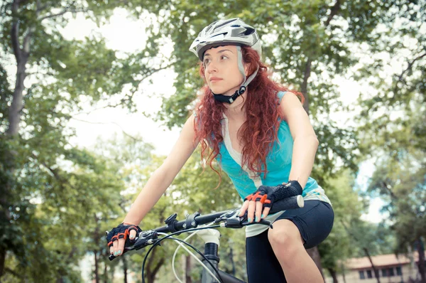 Beautiful redhead girl riding and cycling a bike in a city park — Stock Photo, Image