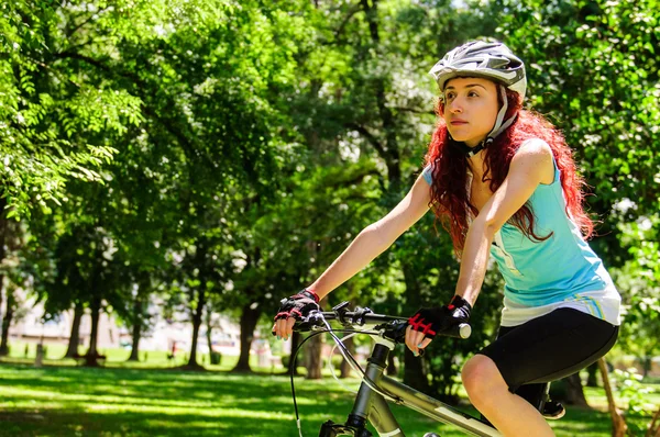 Vacker rödhårig flicka ridning och cykling cykel i en park — Stockfoto