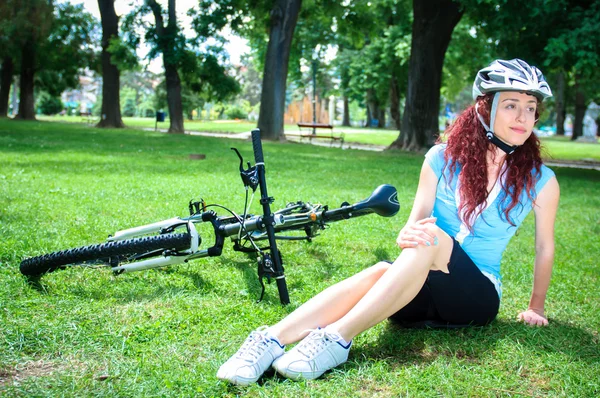 Menina ruiva bonita montando e pedalando uma bicicleta em um parque da cidade — Fotografia de Stock