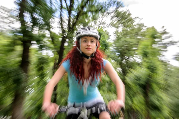 Vacker rödhårig flicka ridning och cykling cykel i en park — Stockfoto