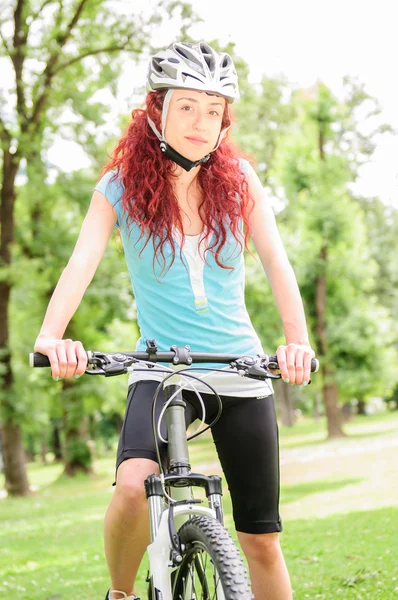 Vacker rödhårig flicka ridning och cykling cykel i en park — Stockfoto