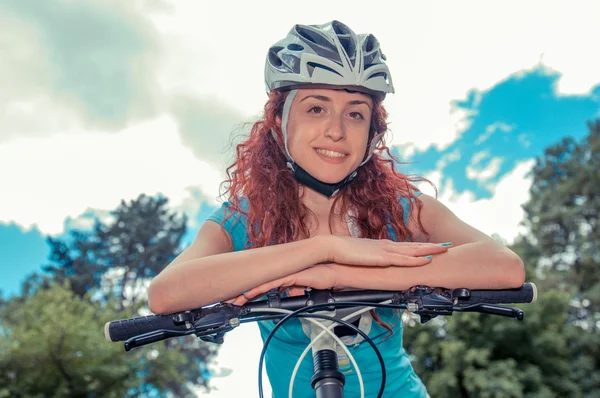 Vacker rödhårig flicka ridning och cykling cykel i en park — Stockfoto