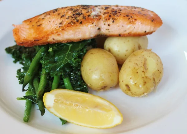 Grilled Atlantic salmon with potatoes, seasonal greens and a lemon wedge — Stock Photo, Image